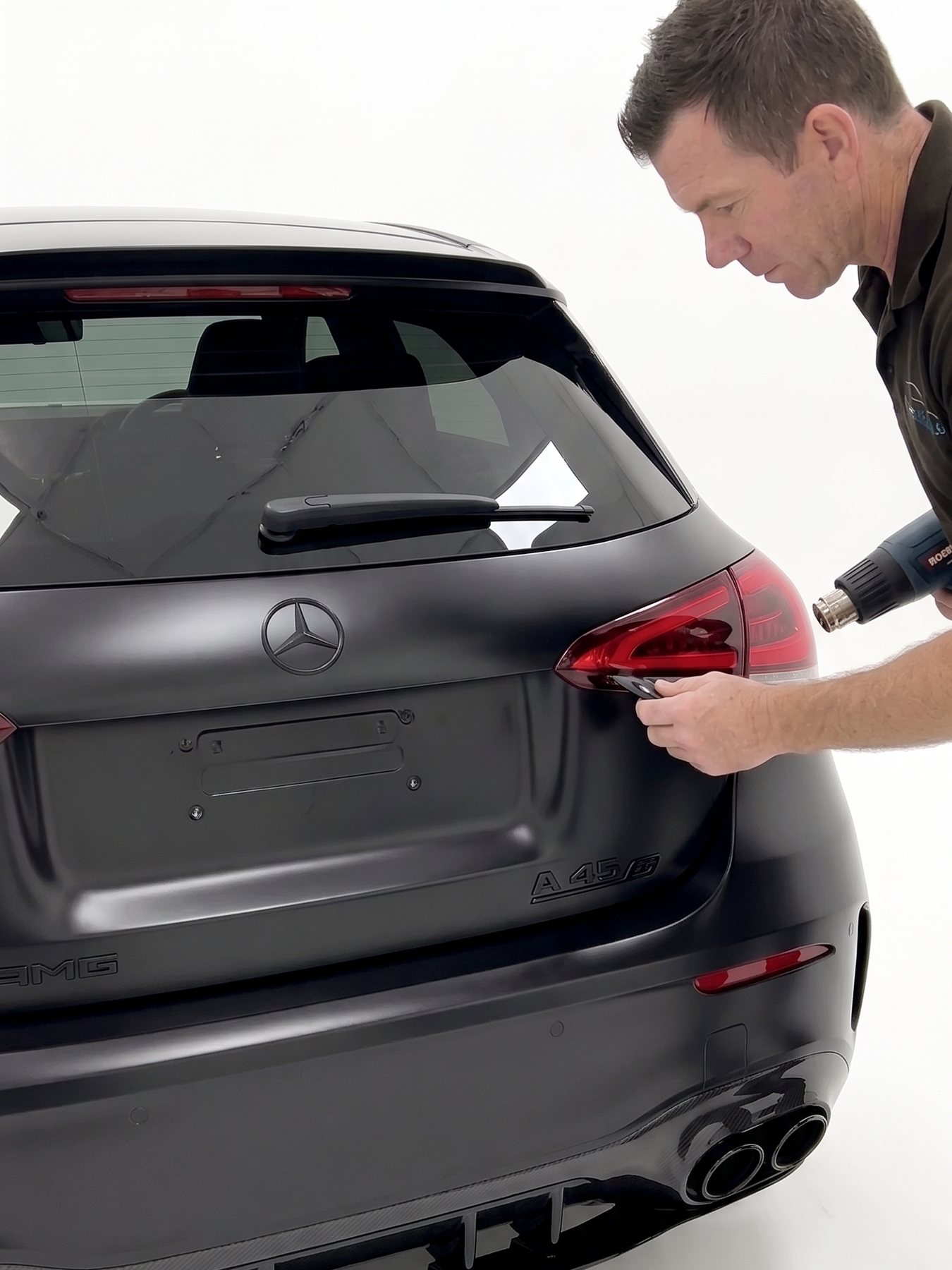 Installer working on rear badges of a matte black hatchback